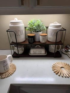 a kitchen counter with coffee cups and mugs on it, next to a plant