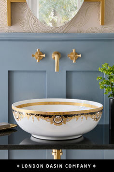 a white bowl sink with gold trim in front of a blue wall and mirror above it