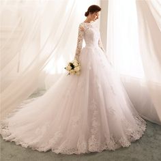 a woman in a white wedding dress standing next to a window with sheer drapes