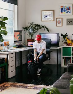 a man sitting in front of a computer desk with a dog on the floor next to him