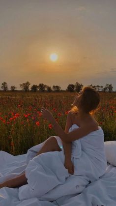 a woman is sitting on a blanket in the middle of a field with poppies