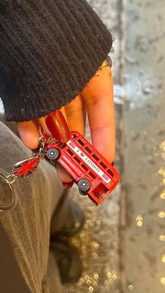 a person holding onto a red bus keychain that is shaped like a car