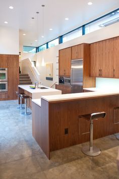 a kitchen with wooden cabinets and white counter tops, stainless steel appliances and stools