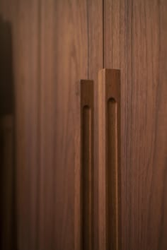 two wooden handles on a door with dark wood grained doors and drawers in the background