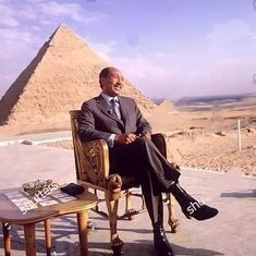 a man sitting in a chair next to a table with an egyptian pyramid in the background