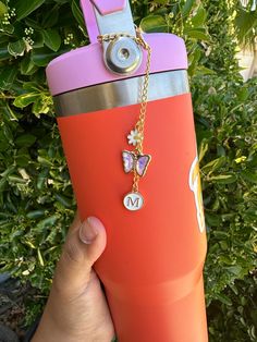 a person holding up a pink and purple water bottle with a butterfly charm on it