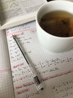 a cup of tea next to an open book and a pen on top of it