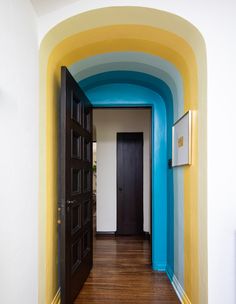 the hallway is painted bright blue, yellow and white with an arched doorway that leads to another room