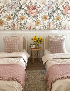 two twin beds with pink and white bedding in front of a floral wallpaper