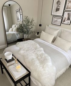 a white bed sitting in a bedroom next to a table with a mirror on it