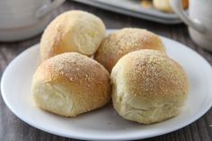 four rolls on a white plate with sugar sprinkled on top and coffee pot in the background