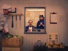 a man standing in front of a mirror cutting vegetables with another man looking at him