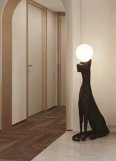 a black cat sitting on the floor next to a white wall with a light on it's head