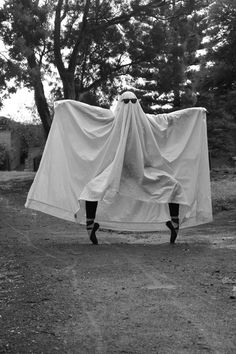 a person standing in the middle of a dirt road holding a white sheet over their head