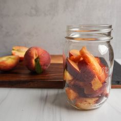 a glass jar filled with sliced peaches on top of a wooden cutting board next to an apple