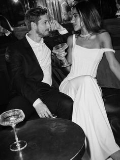 a man and woman sitting next to each other at a table with drinks in front of them