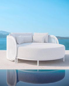 a white couch sitting on top of a swimming pool next to the ocean with pillows