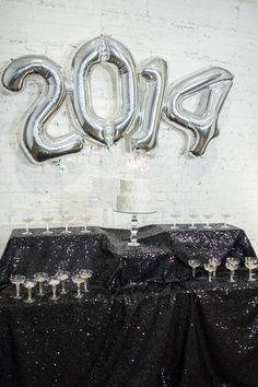 the table is covered with black sequins and has silver balloons in the shape of numbers