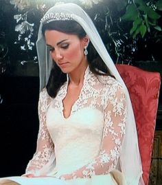 a woman sitting in a red chair wearing a wedding dress and tiara with flowers on it