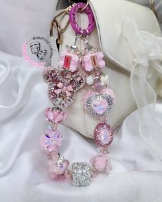 a white purse with pink and silver charms attached to it's side, sitting on a white cloth