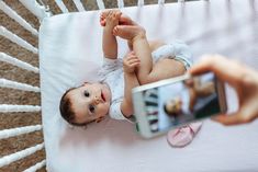 a baby is laying down and taking a photo with his cell phone while being held up by someone's hand