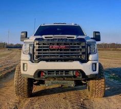 the front end of a white truck parked on top of a dirt road in an open field