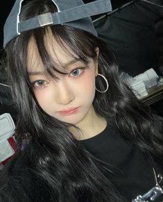 a woman with long black hair wearing a hat and hoop earrings on top of her head