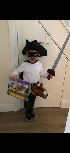 a little boy dressed up as a pirate holding a book and a stuffed animal in his hand