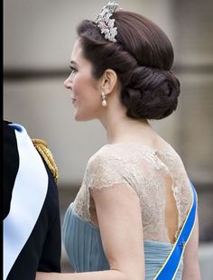 a woman in a blue dress and tiara walking next to a man in a black suit