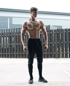 a shirtless man standing in front of a fence with his hands on his hips