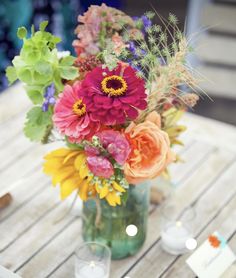 a vase filled with lots of colorful flowers on top of a wooden table next to candles