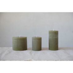 three green candles sitting on top of a white cloth covered table next to each other