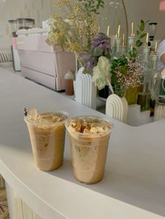 two drinks sitting on top of a white counter next to flowers and vases in the background