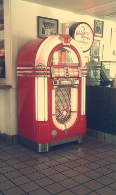 an old fashioned red and white jukebox in a room with pictures on the wall