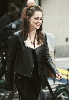 a woman is walking down the street with her hand in her pocket and wearing a black leather jacket