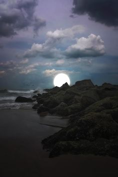 the sun is setting over the ocean with rocks in the foreground and clouds in the background