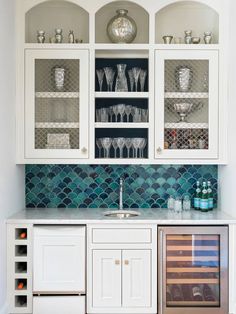 a kitchen with white cabinets and blue tiles on the backsplash, wine bottles in glass cupboards