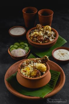 two bowls filled with food sitting on top of a green leaf covered plate next to cups