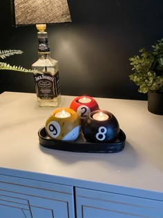 three pool balls on a tray next to a bottle of booze and a lamp