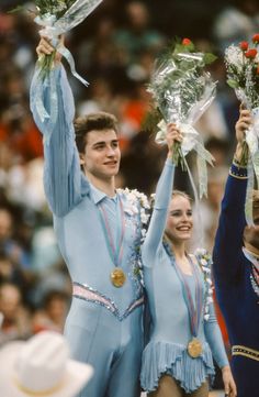 two male and one female figure skaters holding bouquets of flowers in front of an audience