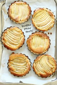 four small pies with slices of apple on top in a baking pan, labeled butter pear tarts