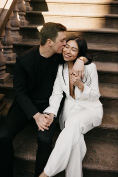 a man and woman sitting on the steps kissing each other with their arms around one another