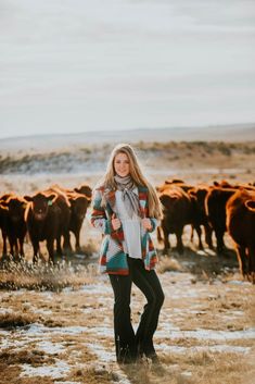 a woman standing in front of a herd of cows on a dry grass covered field