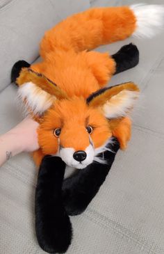 a stuffed fox laying on top of a couch next to a person's hand