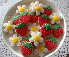 decorated cookies in the shape of strawberries and daisies on a white lace doily