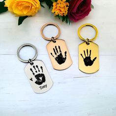 three key chains with handprints on them next to yellow flowers and red roses