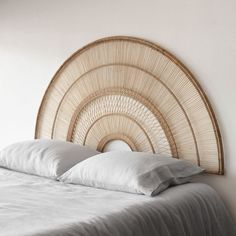 a bed with white sheets and pillows in a room next to a wall mounted wicker headboard