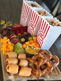 some snacks are sitting on a cutting board with popcorn, pretzels, apples, and other foods