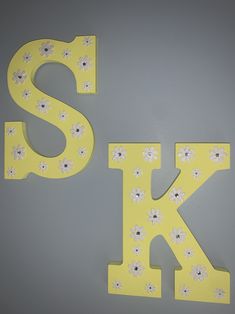 the letters are painted yellow and white with flowers on them to spell the letter k