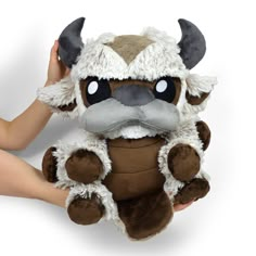 a hand holding a stuffed animal that is brown and white with horns on it's head